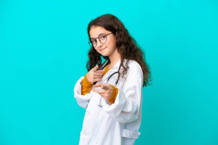 Téléchargez les photos : Petite fille médecin isolé sur fond bleu pointe du doigt vers vous avec une expression confiante - en image libre de droit