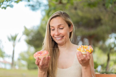 Photo for Young blonde woman at outdoors holding donuts with happy expression - Royalty Free Image