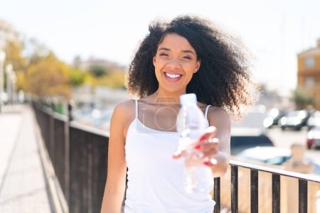 Téléchargez les photos : Jeune femme afro-américaine avec une bouteille d'eau à l'extérieur - en image libre de droit
