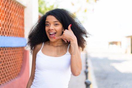 Téléchargez les photos : Jeune femme afro-américaine à l'extérieur faisant un geste téléphonique. Rappelle-moi signe - en image libre de droit