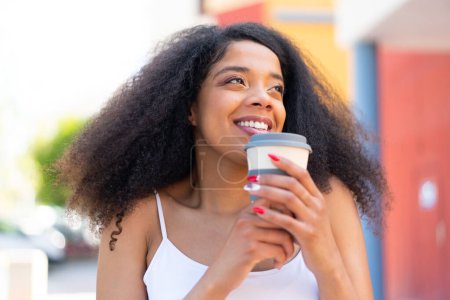 Téléchargez les photos : Jeune femme afro-américaine à l'extérieur tenant un café à emporter - en image libre de droit