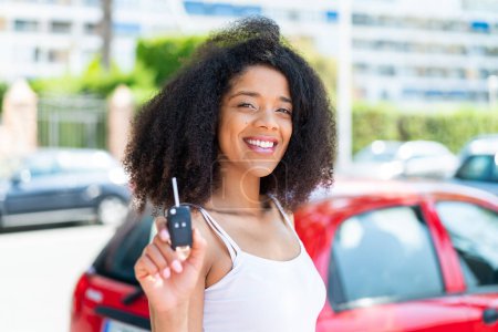 Téléchargez les photos : Jeune femme afro-américaine tenant des clés de voiture à l'extérieur souriant beaucoup - en image libre de droit