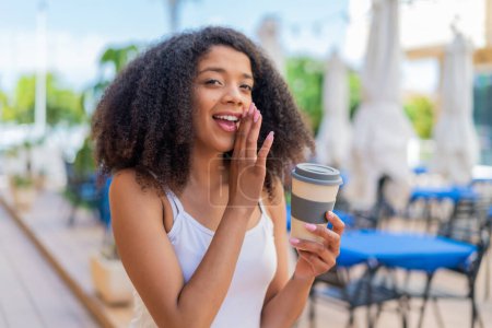 Téléchargez les photos : Jeune femme afro-américaine tenant un café à emporter à l'extérieur chuchotant quelque chose - en image libre de droit