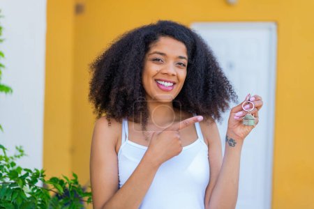 Téléchargez les photos : Jeune femme afro-américaine tenant les clés de la maison à l'extérieur et le pointant - en image libre de droit