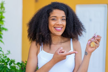 Téléchargez les photos : Jeune femme afro-américaine tenant les clés de la maison à l'extérieur et le pointant - en image libre de droit