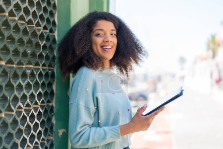 Téléchargez les photos : Jeune femme afro-américaine à l'extérieur tenant une tablette avec une expression heureuse - en image libre de droit