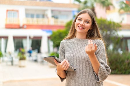 Photo for Young pretty blonde woman holding a tablet at outdoors inviting to come with hand. Happy that you came - Royalty Free Image