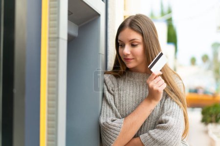 Téléchargez les photos : Jeune jolie femme blonde utilisant un distributeur automatique de billets - en image libre de droit