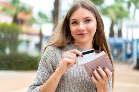 Téléchargez les photos : Jeune jolie femme blonde tenant portefeuille et carte de crédit avec expression heureuse - en image libre de droit