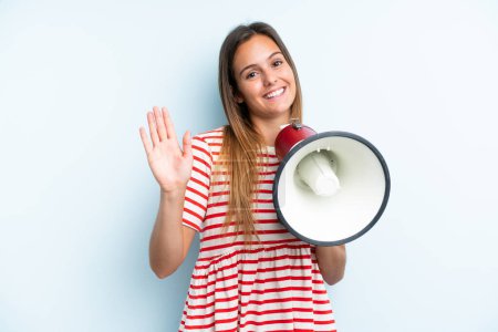 Photo for Young caucasian woman isolated on blue background holding a megaphone and saluting with hand with happy expression - Royalty Free Image