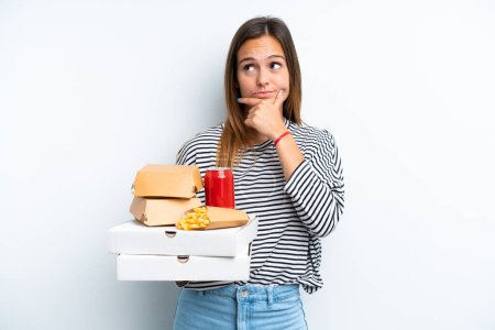 Téléchargez les photos : Young caucasian woman holding fast food isolated on white background having doubts - en image libre de droit