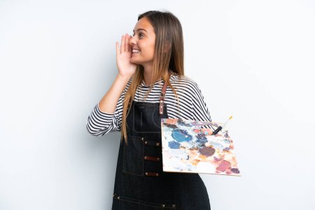 Téléchargez les photos : Jeune artiste femme caucasienne tenant une palette isolée sur fond blanc criant avec la bouche grande ouverte sur le côté - en image libre de droit