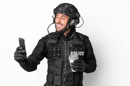 Photo for SWAT caucasian man isolated on white background holding coffee to take away and a mobile - Royalty Free Image