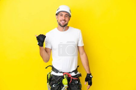 Téléchargez les photos : Jeune grimpeur isolé sur fond jaune pointant vers le côté pour présenter un produit - en image libre de droit
