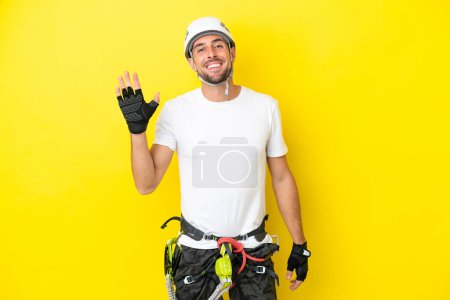 Téléchargez les photos : Jeune alpiniste isolé sur fond jaune saluant à la main avec une expression heureuse - en image libre de droit