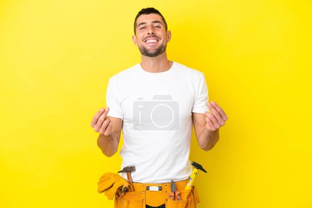 Foto de Joven electricista caucásico hombre aislado en amarillo fondo haciendo dinero gesto - Imagen libre de derechos
