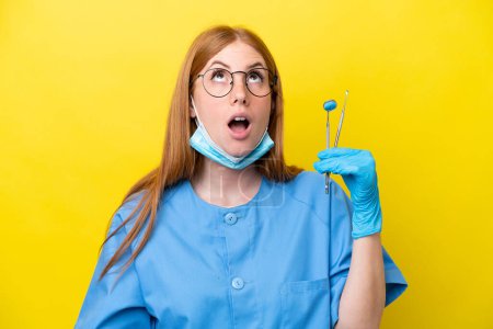 Téléchargez les photos : Jeune rousse Dentiste femme isolée sur fond jaune levant les yeux et avec une expression surprise - en image libre de droit