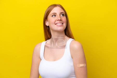 Photo for Young redhead woman wearing a band-aids isolated on yellow background looking up while smiling - Royalty Free Image