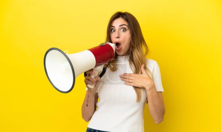 Photo for Caucasian woman isolated on yellow background shouting through a megaphone with surprised expression - Royalty Free Image