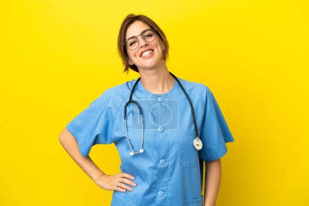 Photo for Surgeon doctor woman isolated on yellow background posing with arms at hip and smiling - Royalty Free Image