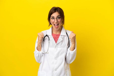 Photo for Doctor woman isolated on yellow background celebrating a victory in winner position - Royalty Free Image
