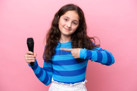 Photo for Little singer girl picking up a microphone isolated on pink background and pointing it - Royalty Free Image