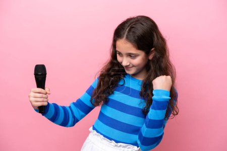 Téléchargez les photos : Petite chanteuse ramassant un microphone isolé sur fond rose célébrant une victoire - en image libre de droit