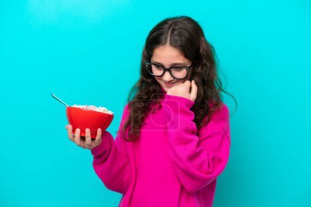 Photo for Little girl holding a bowl of cereals isolated on blue background celebrating a victory - Royalty Free Image
