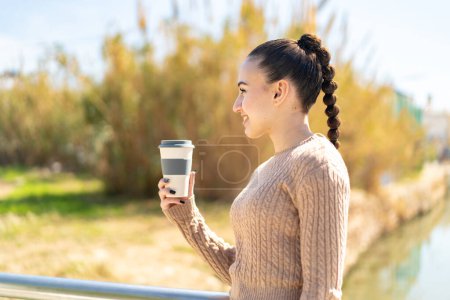 Téléchargez les photos : Jeune fille marocaine tenant un café à emporter à l'extérieur avec une expression heureuse - en image libre de droit