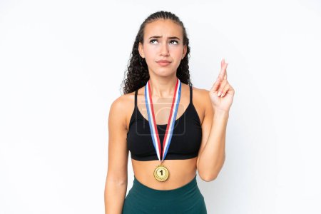 Foto de Joven deportista con medallas aisladas sobre fondo blanco con dedos cruzando y deseando lo mejor - Imagen libre de derechos
