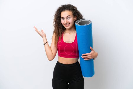 Photo for Young sport Arab woman going to yoga classes while holding a mat isolated on white background extending hands to the side for inviting to come - Royalty Free Image
