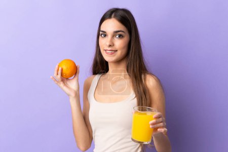 Téléchargez les photos : Jeune femme caucasienne isolée sur fond violet tenant une orange et un jus d'orange - en image libre de droit