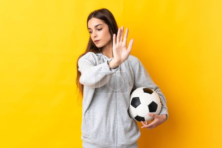 Téléchargez les photos : Jeune joueuse de football isolée sur fond jaune faisant geste d'arrêt et déçue - en image libre de droit