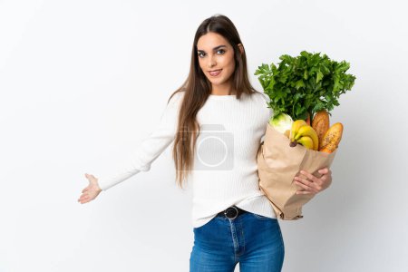 Téléchargez les photos : Jeune femme caucasienne achetant de la nourriture isolée sur fond blanc étendant les mains sur le côté pour inviter à venir - en image libre de droit