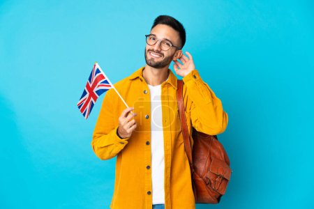 Foto de Joven hombre caucásico sosteniendo una bandera del Reino Unido aislado sobre fondo amarillo que tiene dudas - Imagen libre de derechos