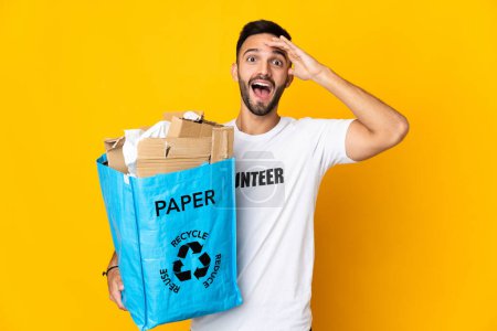 Foto de Joven hombre caucásico sosteniendo una bolsa de reciclaje llena de papel para reciclar aislado sobre fondo blanco con expresión sorpresa - Imagen libre de derechos