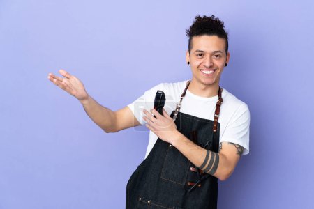 Téléchargez les photos : Barbier dans un tablier sur fond violet isolé étendant les mains sur le côté pour inviter à venir - en image libre de droit