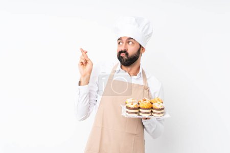 Photo for Young man holding muffin cake over isolated white background with fingers crossing and wishing the best - Royalty Free Image