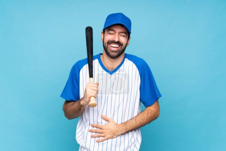 Foto de Joven jugando béisbol sobre fondo azul aislado sonriendo mucho - Imagen libre de derechos