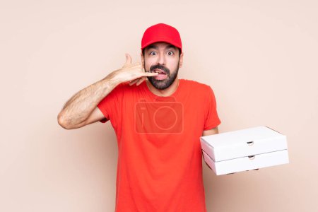 Téléchargez les photos : Jeune homme tenant une pizza sur fond isolé faire un geste téléphonique et douter - en image libre de droit