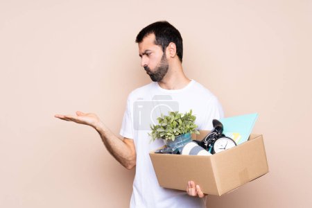 Foto de Hombre sosteniendo una caja y moviéndose en un nuevo hogar sobre un fondo aislado sosteniendo el copyspace con dudas - Imagen libre de derechos
