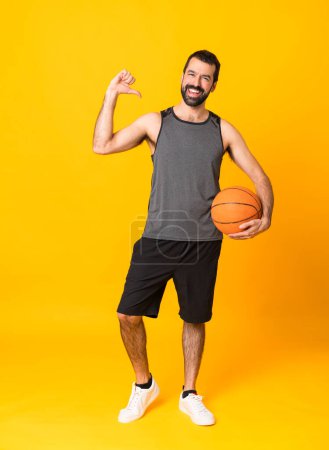 Photo for Full-length shot of man over isolated yellow background playing basketball and proud of himself - Royalty Free Image