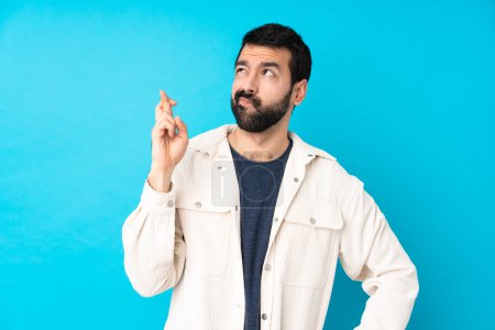 Photo for Young handsome man with white corduroy jacket over isolated blue background with fingers crossing and wishing the best - Royalty Free Image