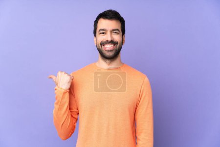 Foto de Caucásico guapo hombre sobre aislado púrpura fondo apuntando a un lado para presentar un producto - Imagen libre de derechos