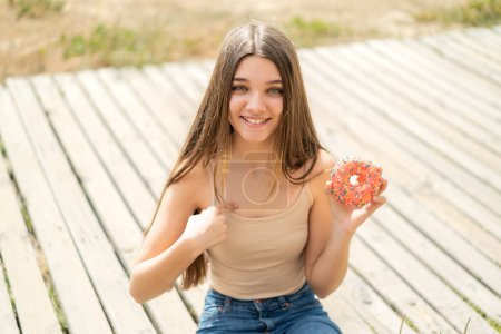 Photo for Teenager girl holding a donut at outdoors with surprise facial expression - Royalty Free Image