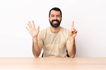 Photo for Caucasian man with beard in a table counting six with fingers. - Royalty Free Image