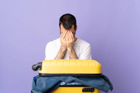 Téléchargez les photos : Voyageur homme caucasien avec une valise pleine de vêtements sur fond violet isolé avec expression fatiguée et malade - en image libre de droit