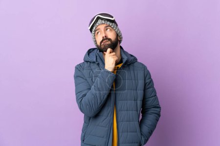 Foto de Hombre esquiador con gafas de snowboard sobre fondo púrpura aislado teniendo dudas y pensando - Imagen libre de derechos