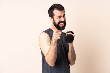 Photo for Caucasian sport man with beard making weightlifting over isolated background surprised and pointing front - Royalty Free Image