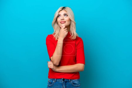 Photo for Young Russian woman isolated on blue background having doubts while looking up - Royalty Free Image